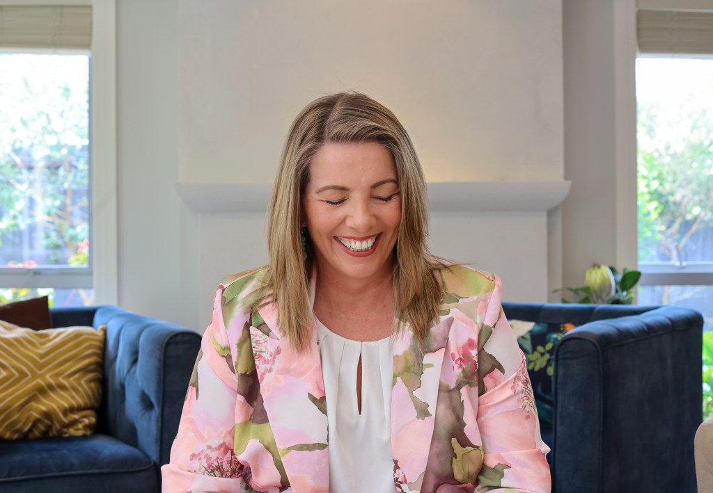 Vanessa Ronan-Pearce laughing on a blue sofa in a floral jacket
