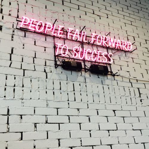 A neon sign on a brick wall reading People fail forward to success.